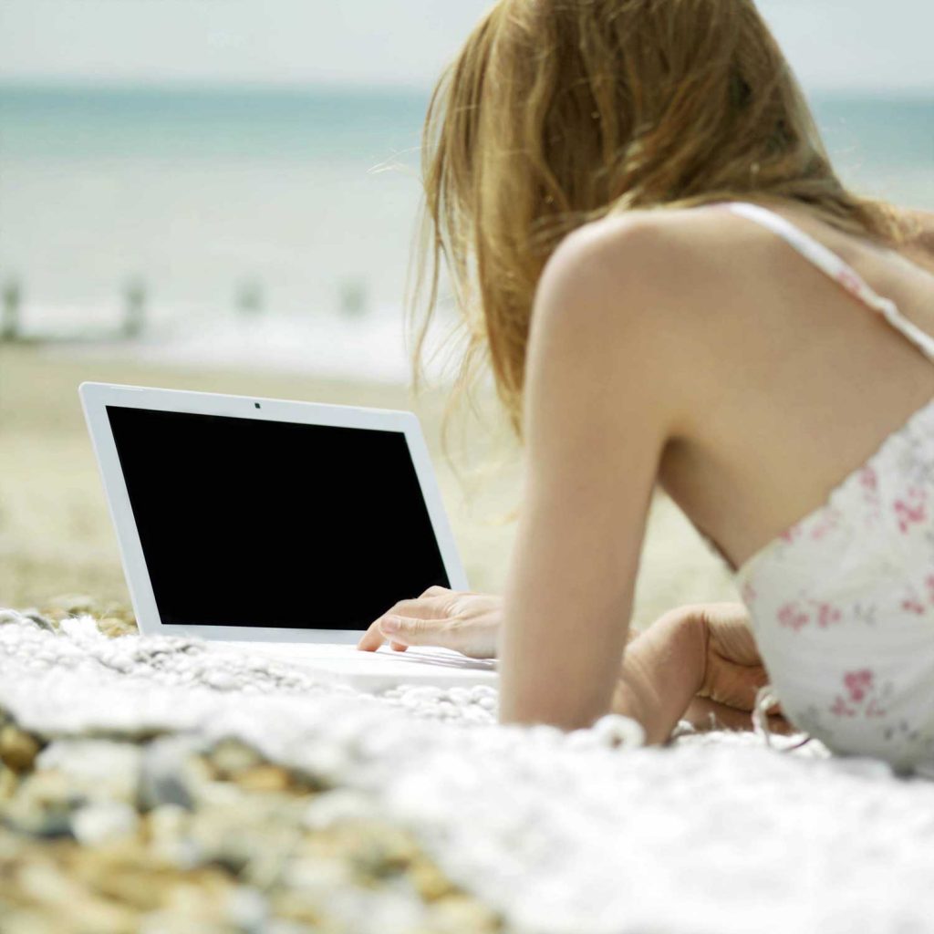 Eine Autorin mit Laptop am Strand.