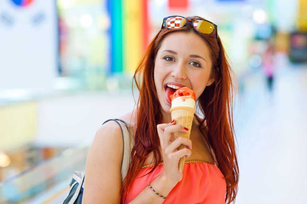 Frau mit Sonnenbrille, die genüsslich ein Eis isst.