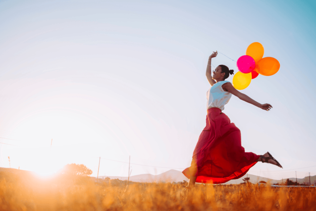 Eine Frau mit Luftballons springt freudig über ein Feld im Sonnenuntergang